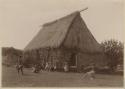Thatched chief's house with people in front of it, including men with weapons