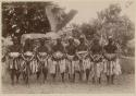 Group of male dancers outside, leaning on clubs