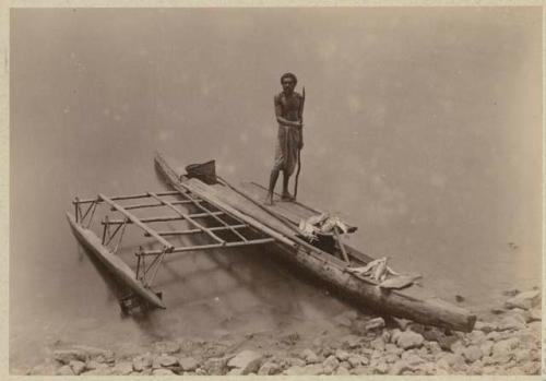 Man standing in double canoe with fish in it