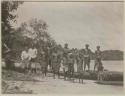 Men and boys lined up at shore in front of double canoe