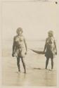 Two women standing on shore, boat in background