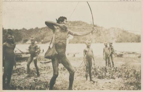 Man aiming bow and arrow, shore and boys watching in background