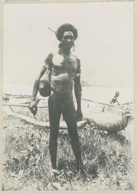 Man standing on shore in front of canoes, child in background