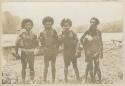 Five men standing on shore in front of canoes