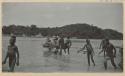 People in outrigger canoes and standing in water at shore