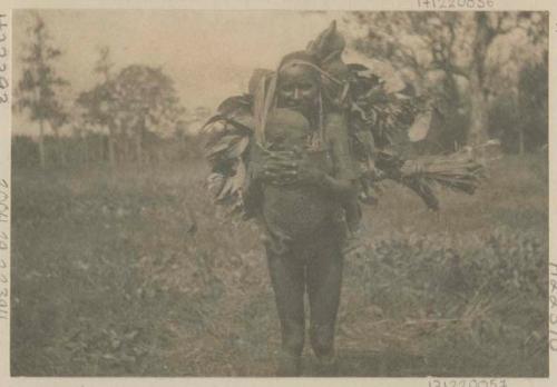 Woman standing outside, with bundle on back and baby in carrier