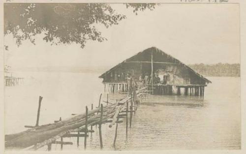 People inside thatched structure on stilts in the water, with one person leaving structure via bridge