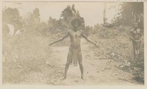 Man standing outside with arms spread, in the background another man and a Western man with net [Barbour?]