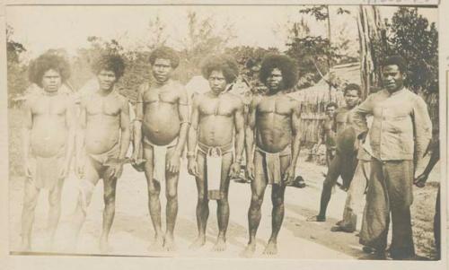 Men standing in a row outside, in front of houses