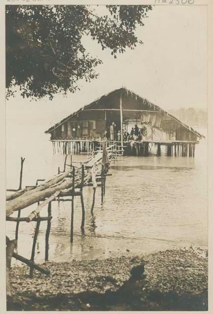 People inside thatched structure on stilts in the water, with bridge