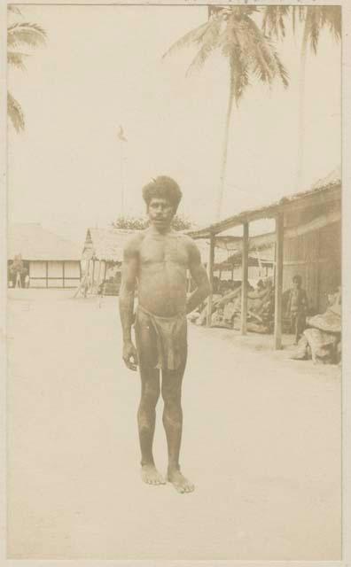 Man standing outside, structures and people in background