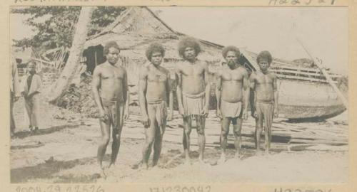 Row of men in front of structures