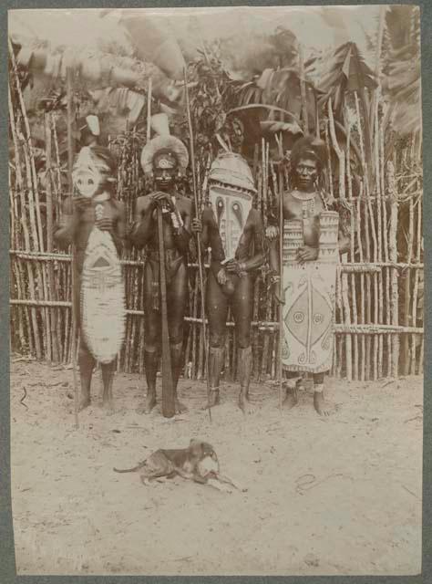 Men holding carved shields in front of fence