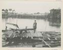 Woman standing on raft with equipment for washing sago, people in canoe in background