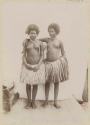 Posed photograph of two women standing in grass skirts