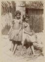 Two women standing outside in grass skirts