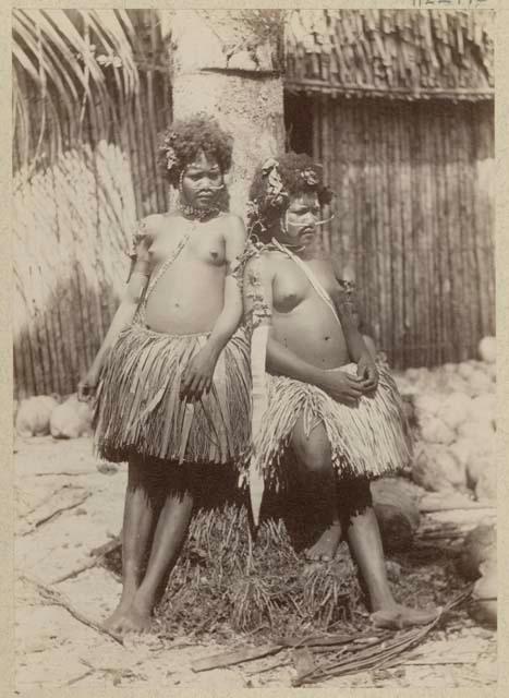 Two women standing outside in grass skirts