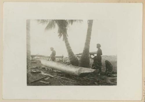 Men carving wood on beach