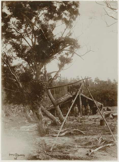 Native encampment with trees, building, children, and dogs