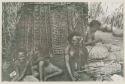 Man, woman and two children sitting in front of thatched structure