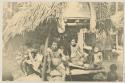 Group of men and children sitting in front of house