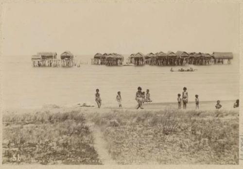 People along shore, with marine village in background