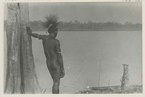 Man beside tree looking out over water, rear view