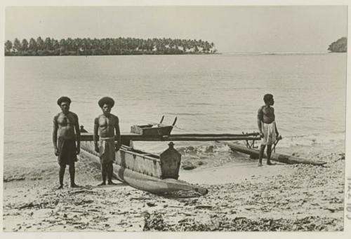 Men on riverbank beside outrigger canoe