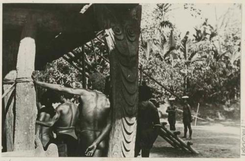 Men's backs and carved post supporting building