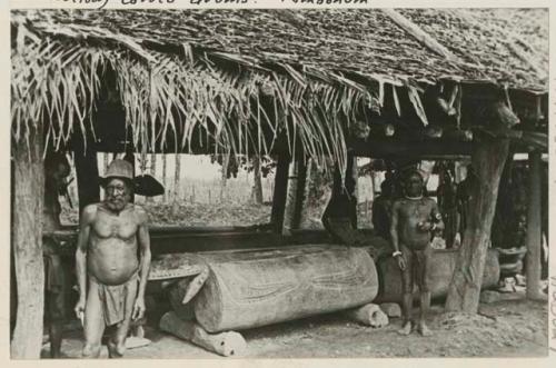 Men beside carved drums under roof