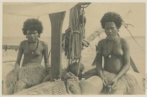 Two women seated on boat next to furled sail and rope