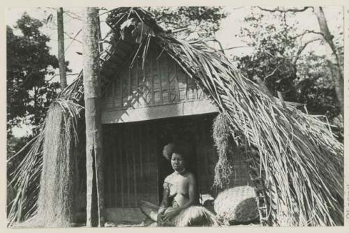 Woman seated beside woven basket on porch of small building