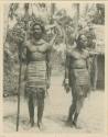 Two chiefs standing, wearing intricately woven aprons