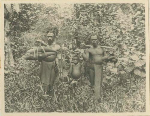 Two men and a boy carrying vegetables, yams and coconuts from their garden