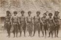 Group of men standing in front of a thatched structure