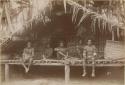 Three people sitting on a platform in front of a house