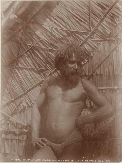 Man with a basket standing in front of thatched structure