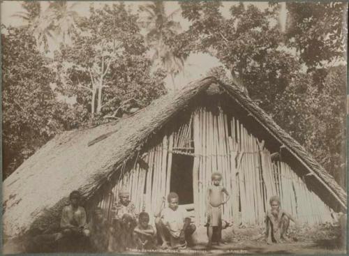 Children and men standing by a thatched "A" frame structure