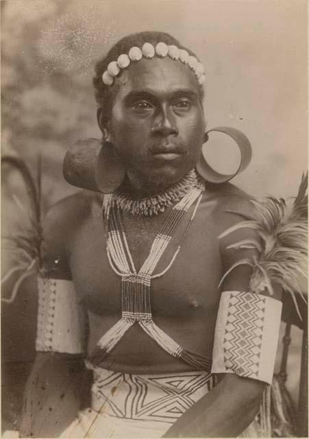 Studio portrait of man wearing beads, shells, feathers and large tortoise shell earrings