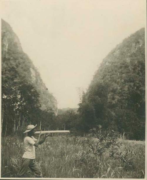 Man with hat in field, holds tube to mouth