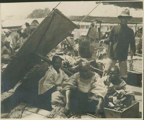 Three women under wicker awning, man behind