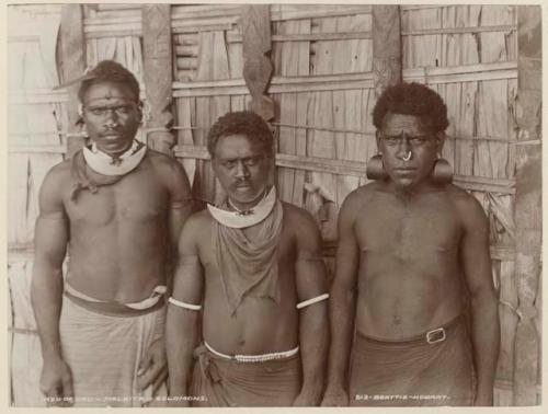 Three men of Uru standing in front of thatched structure