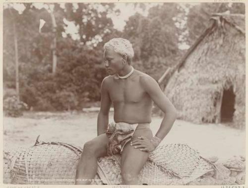 Young man sitting on woven mats on rock wall at Nukapu