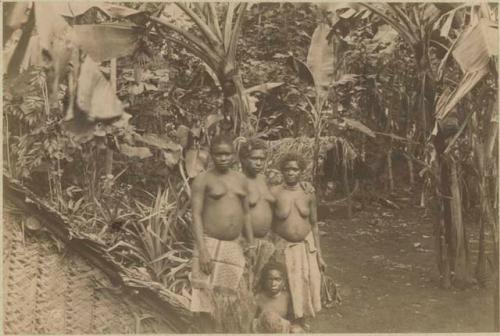 Three women and a child next to a thatched hut