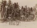 Man and children with canoe on beach, houses in background