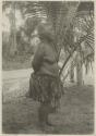 Woman standing in front of palm, side view