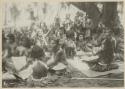 Group sitting under tree, with woven mats covering their legs