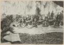 Group sitting under tree, with woven mats covering their legs