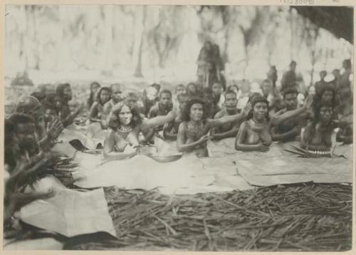 Group sitting under tree, with woven mats covering their legs