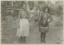 Two women carrying a bundle tied to a pole